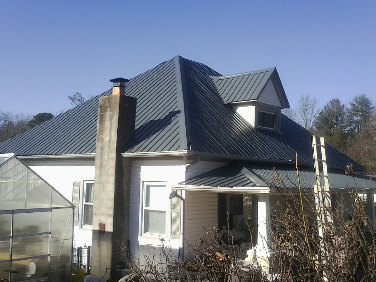 Dark blue standing seam metal roof on a white farmhouse with dormer — Slate & Tile Roof Repair by Roofing Brothers in Van Vleck