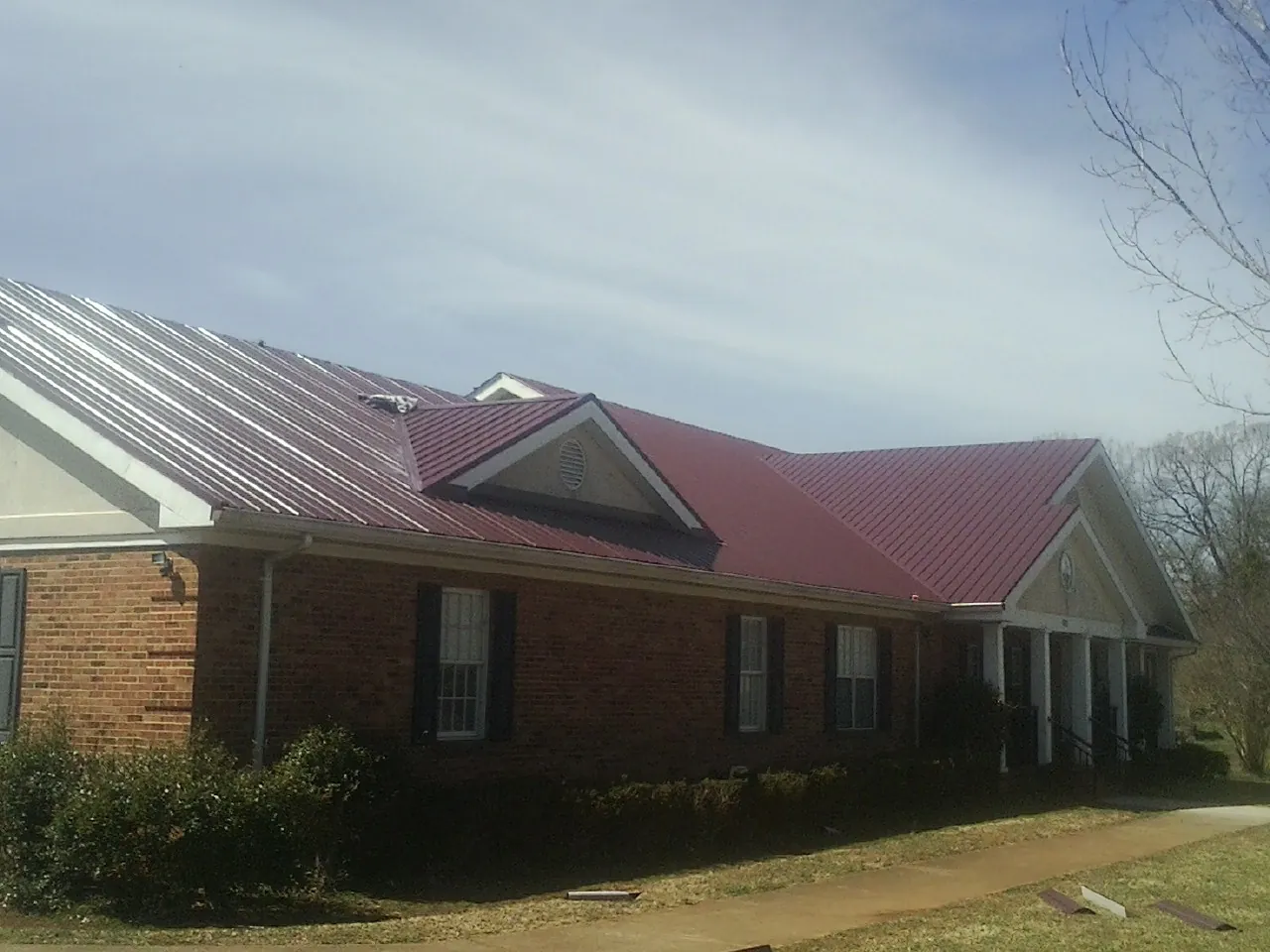 Red metal roof with gabled entries on a long brick building, from a Hail Damage Roof Repair job in Van Vleck