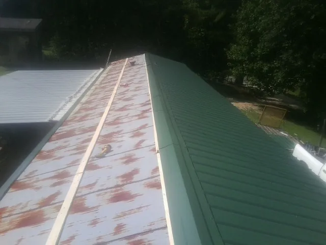 Old rusted panels beside newly installed green metal roofing — Wind Damage Roof Repair by Roofing Brothers in Van Vleck