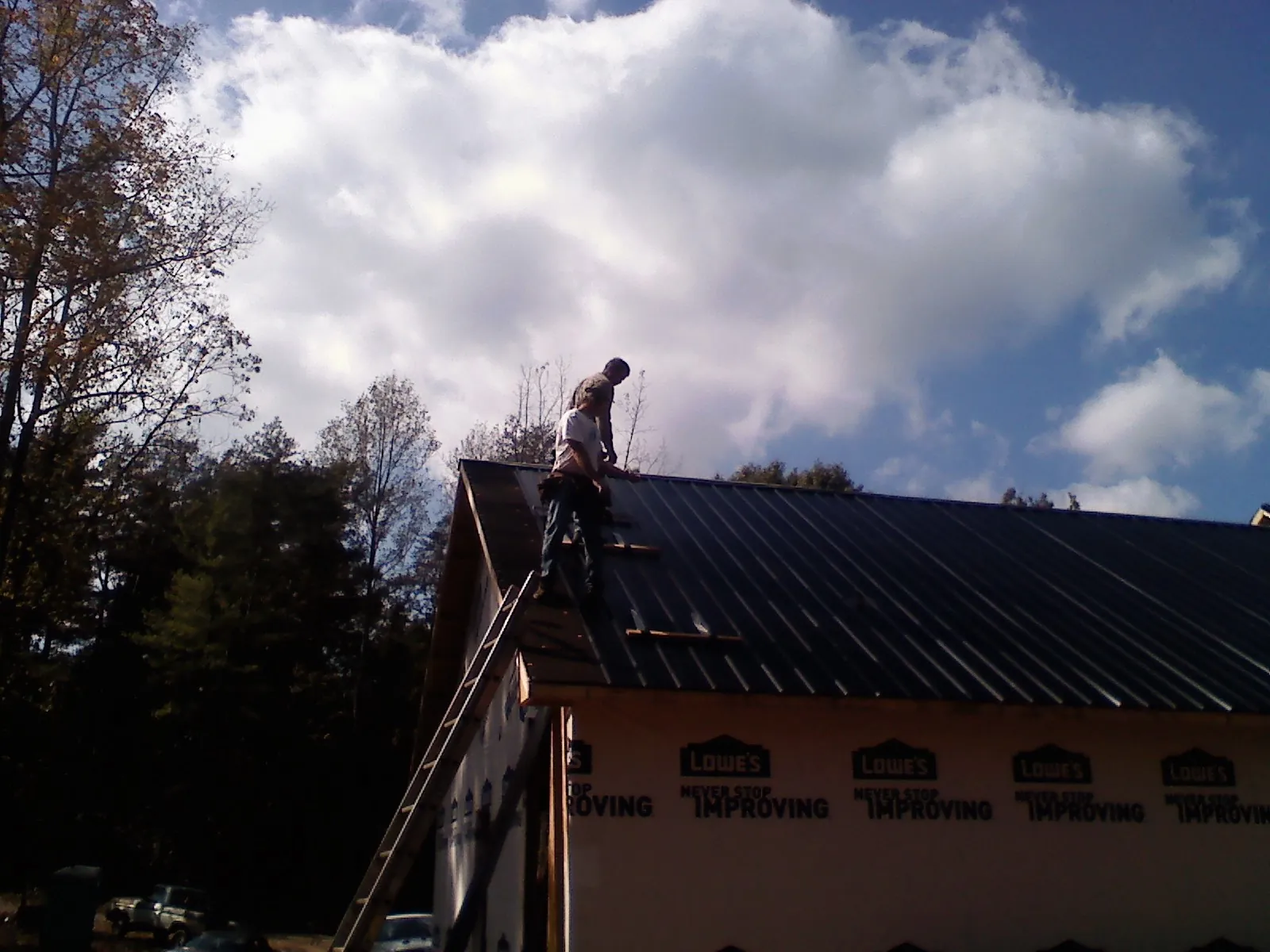Roofer fastening dark metal panels high against a cloudy sky, from a Roof Inspection job in Van Vleck