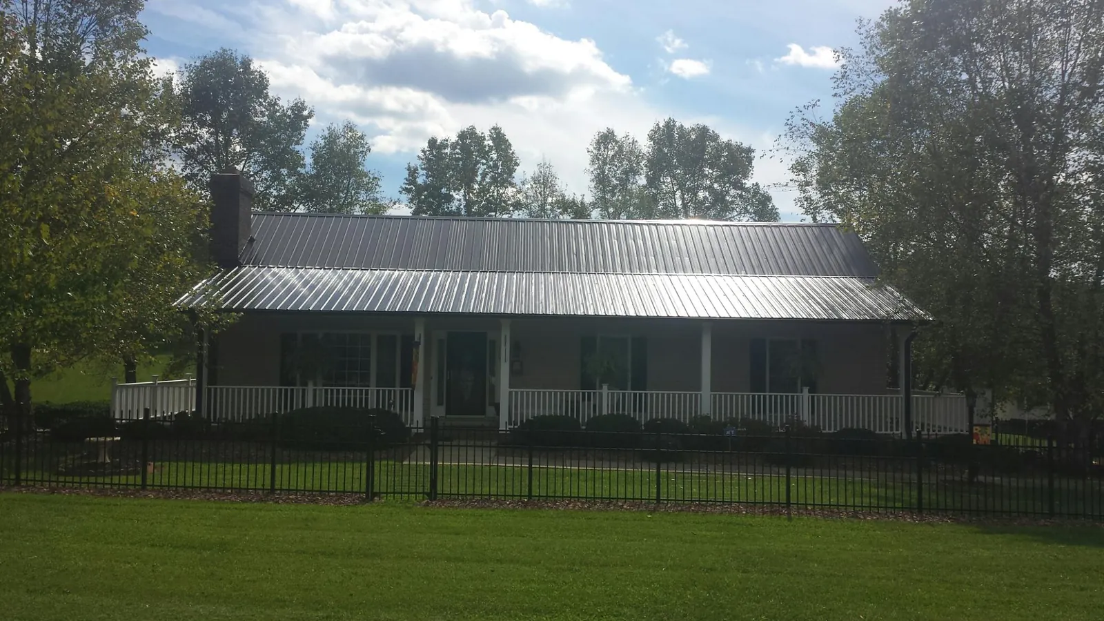 Gray metal roof on a brick ranch with a full width front porch — Gutter Guard Installation work by our crew in Van Vleck