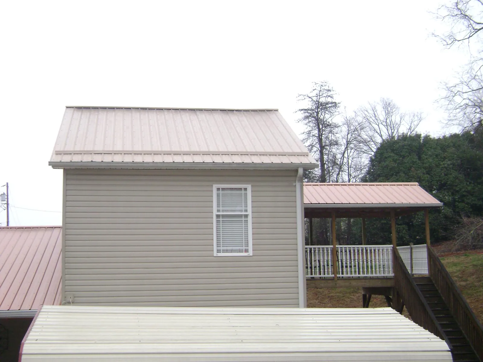 Tan metal roofs on a two story addition and attached porch, from a Roof Replacement job in Van Vleck